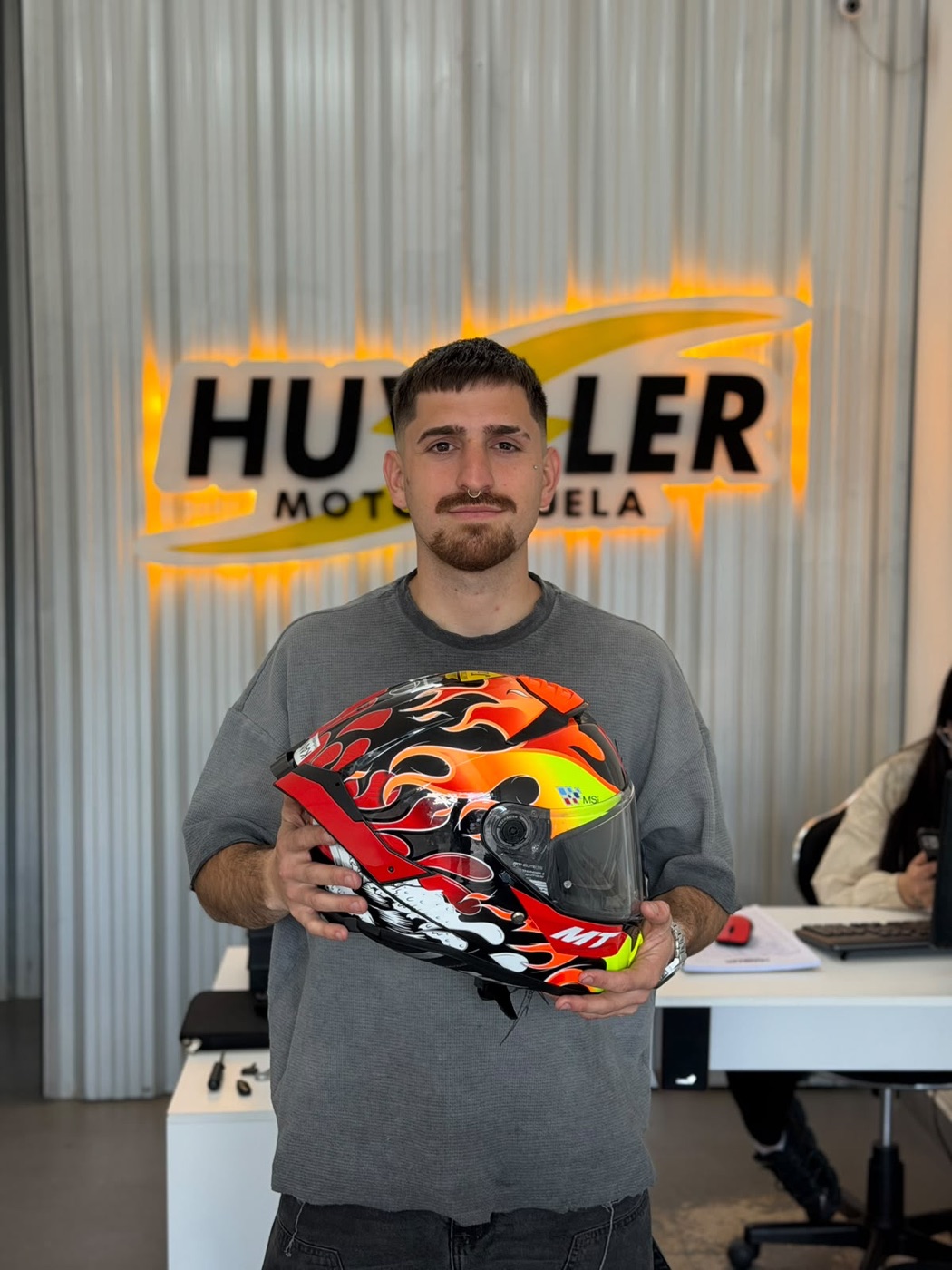 El profe de Huviller Motoescuela con un casco, frente al cartel iluminado de la escuela